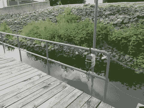 A hydrophone system encased in a tupperware container attached to the metal railing of a wooden dock on the Mississippi river bank.