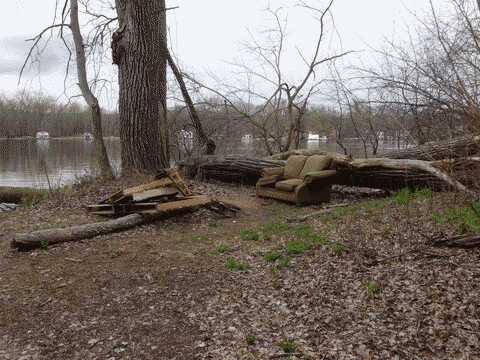 a couch by the riverbank, set up next to a fire pit